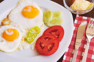 Breakfast - fried eggs, butter and tomato in white plate. Close up image.