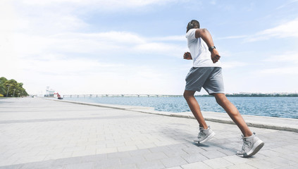 Afro Man Jogging Along River Bank In City. Panorama, Rear View