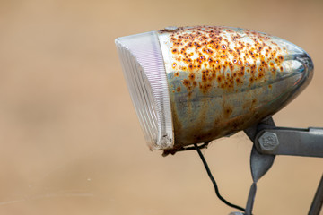 Fototapeta na wymiar Alte rostige Fahrradlampe mit Frontreflektor vor schönem unscharfen Hindlampe mit Frontreflektor vor schönem unscharfen Hintergrund lädt zum gemütlichen Radeln und Fahrradfahren ein