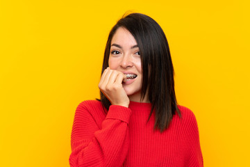 Young Mexican woman with red sweater over yellow wall nervous and scared