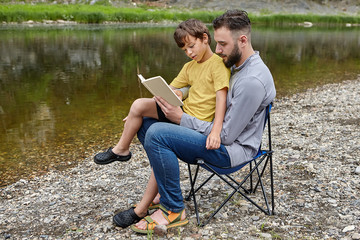 Father is reading a book to his son in nature.