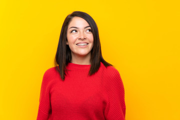 Fototapeta premium Young Mexican woman with red sweater over yellow wall laughing and looking up