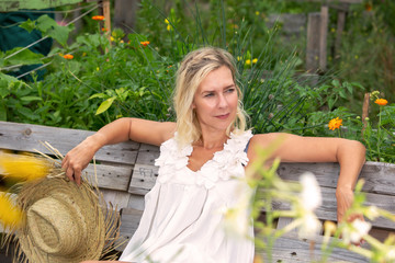Obraz premium beautiful blonde woman in white dress sitting outside in garden