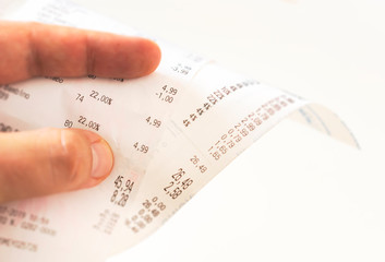 human fingers holding a paper receipt with the bill of charges and checking the total amount.