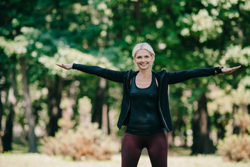 attractive, smiling mature sportswoman looking at camera while training in park