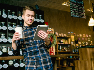 Fototapeta na wymiar guy with coffee paper cup and tablet in cafe 