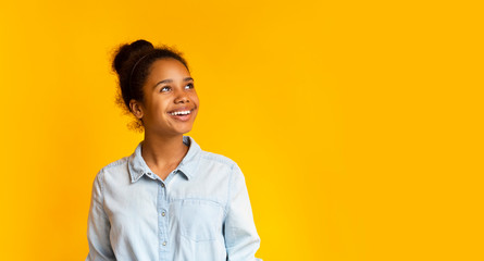 Pensive girl looking upwards at empty space on yellow background