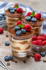 Classic tiramisu dessert with blueberries and raspberries in a glass and napkin on concrete background