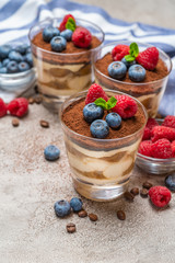 Classic tiramisu dessert with blueberries and raspberries in a glass and napkin on concrete background