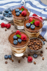 Classic tiramisu dessert with blueberries and raspberries in a glass and napkin on concrete background