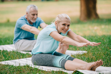 Fototapeta premium selective focus of smiling, mature man and woman sitting in stretching poses while practicing yoga in park