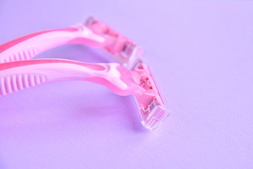 New pink disposable razors for safe shaving of female skin with selective focus on purple background with copy space. Razor for smooth shaving. Sharp razors for personal hygienic routine 