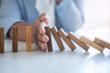 Fotobehang Risk and Strategy in Business, Image of hand stopping falling collapse wooden block dominoes effect from continuous toppled block, prevention and development to stability © Ngampol