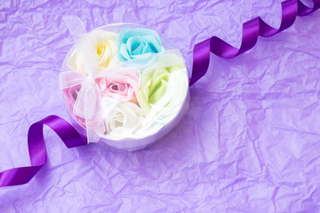 Rose flowers shaped scented soap petals in transperent round box on crimpled violet paper background. Handcrafted soap petals.