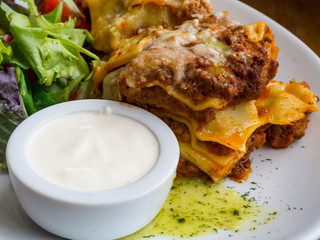 Tasty serving of traditional Italian lasagne with spicy tomato based ground beef and melted mozzarella cheese between layers of noodles, with cream and green leafs