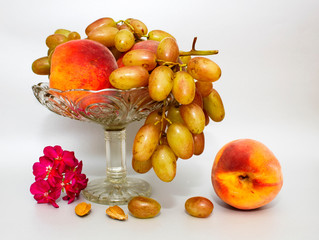 Still life with fruit peaches and grapes on a glass vase on a grey or silver background
