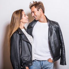 Young beautiful couple in black leather jackets pose in studio.