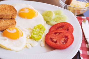 Breakfast - fried eggs, butter and tomato in white plate. Close up image