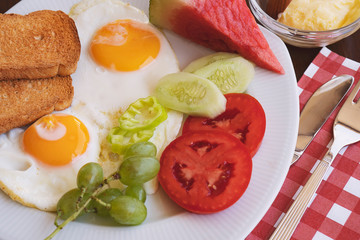 Breakfast - fried eggs, butter and tomato in white plate. Close up image