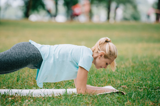 attractive mature woman doing plank exercise while racticing yoga on green lawn in park - Powered by Adobe