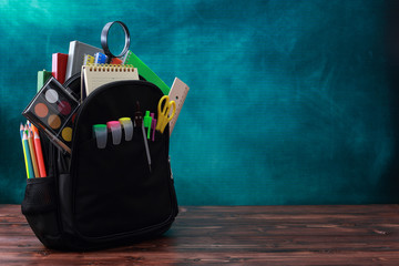 Back to school concept. School bag, pencils, crayons, scissor, notebooks, alarm clock, eraser, markers, watermark, ruler, pencil sharpener, magnifying glass in a combine with a cyan background