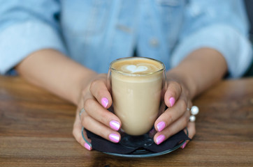 A glass of cappuccino in female hands