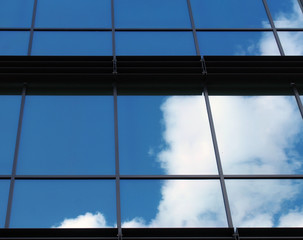 clouds and bright blue sky reflected in the square mirrored windows of a modern commercial office building
