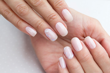 Beautiful groomed woman's hands with feminine nails on the light gray background.