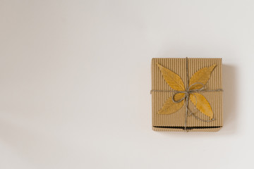 craft gift box, tied with string with a bow and autumn fallen leaves on a beige background. Birthday gift for people born in autumn. The view from the top. Copy space