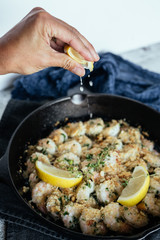 Woman's hand squeezing fresh lemon juice on shrimp scampi