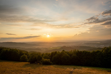 Fototapeta premium Sunset with view on landscape with fully colored clouds orange and purple and sun behind it and city Valasske Mezirici captured during summer late time.