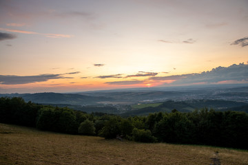 Sunset with view on landscape with fully colored clouds orange and purple and sun behind it and city Valasske Mezirici captured during summer late time.