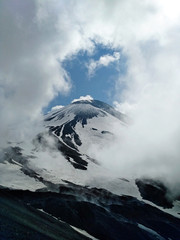 Volcanic mountain with black slopes with white snow and natural clouds frame.