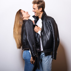 Young beautiful couple in black leather jackets pose in studio.