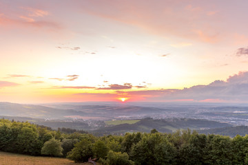 Sunset with view on landscape with fully colored clouds and orange sun goes down and city Valasske Mezirici captured during summer late time