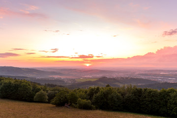 Sunset with view on landscape with fully colored clouds and orange sun goes down and city Valasske Mezirici captured during summer late time