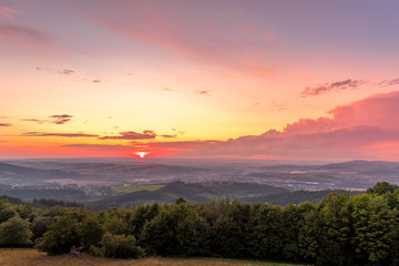 Sunset with view on landscape with fully colored clouds and orange sun goes down and city Valasske Mezirici captured during summer late time