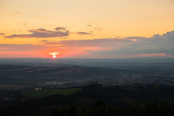 Sunset with view on landscape with fully colored clouds and orange sun goes down and city Valasske Mezirici captured during summer late time