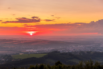 Sunset with view on landscape with fully colored clouds and orange sun goes down and city Valasske Mezirici captured during summer late time