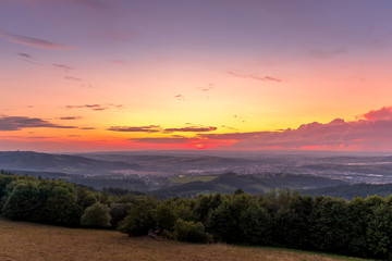Landscape sunset with fully colored clouds pink orange sky look on meadow close to city Valasske Mezirici captured during summer late time.