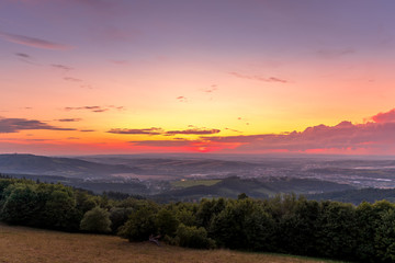Landscape sunset with fully colored clouds pink orange sky look on meadow close to city Valasske Mezirici captured during summer late time.