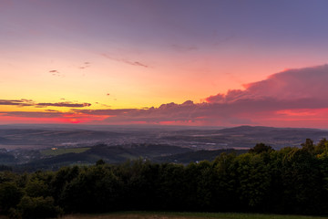 Landscape sunset with fully colored clouds pink orange sky look on meadow close to city Valasske Mezirici captured during summer late time.