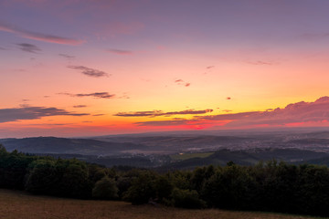 Landscape sunset with fully colored clouds pink orange sky look on meadow close to city Valasske Mezirici captured during summer late time.