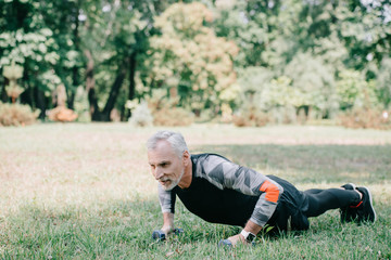 smiling mature sportsman doing push ups with barbells on green lawn