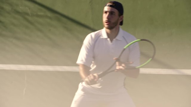 Fit young man playing tennis on a hardcourt outdoors. Professional player hitting forehands on tennis court.