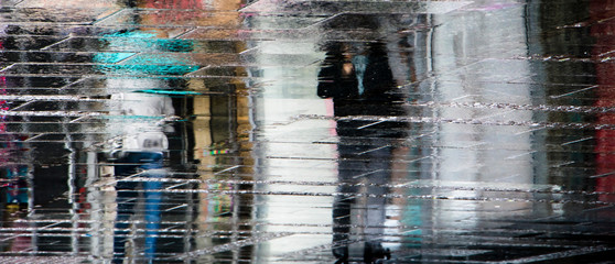 Blurry reflection shadow silhouettes of peope walking alone under umbrella