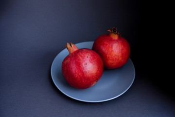  ripe red pomegranate on a gray plate on a black background