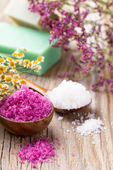 Sea salt in bowl, aroma oil in bottles, Wellness and flowers on grey textured background and flowers on vintage wooden background. Selective focus.