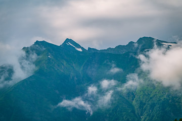 Green slopes and rocky peaks of high mountains in cloudy summer day