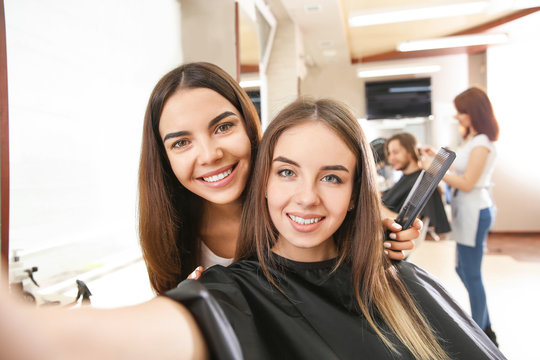 Young woman taking selfie with her hairdresser in salon